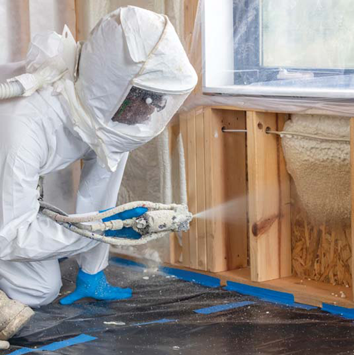 Technician in protective gear applying spray foam insulation.